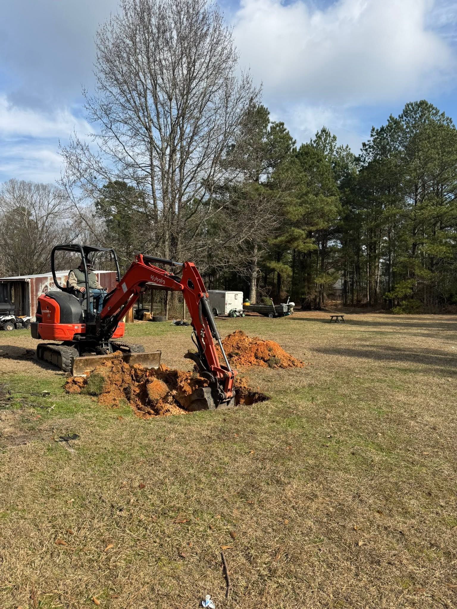 Orange excavator digging a hole in a grassy yard near trees and a house