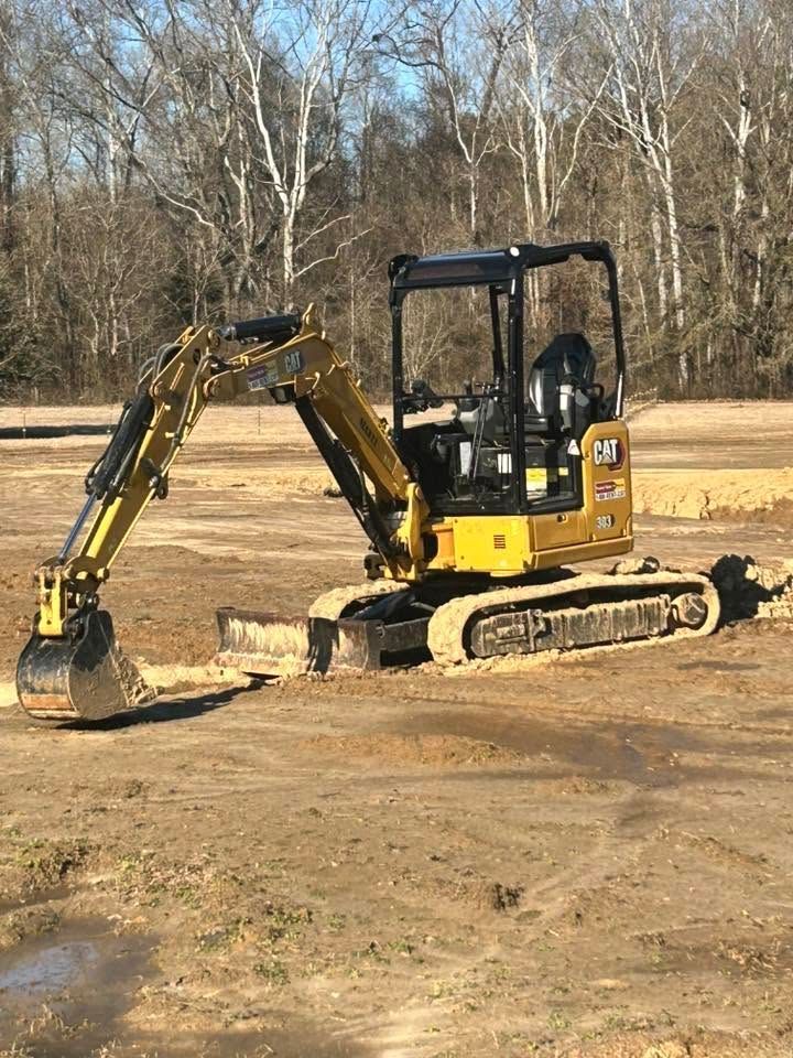 Yellow mini excavator on tracks digging dirt in a bare wooded field