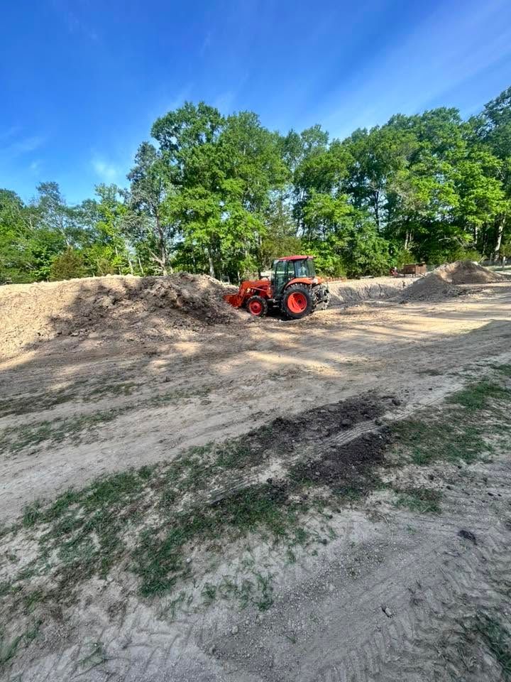 Red tractor on a dirt mound in a sunny field with trees and blue sky in the background