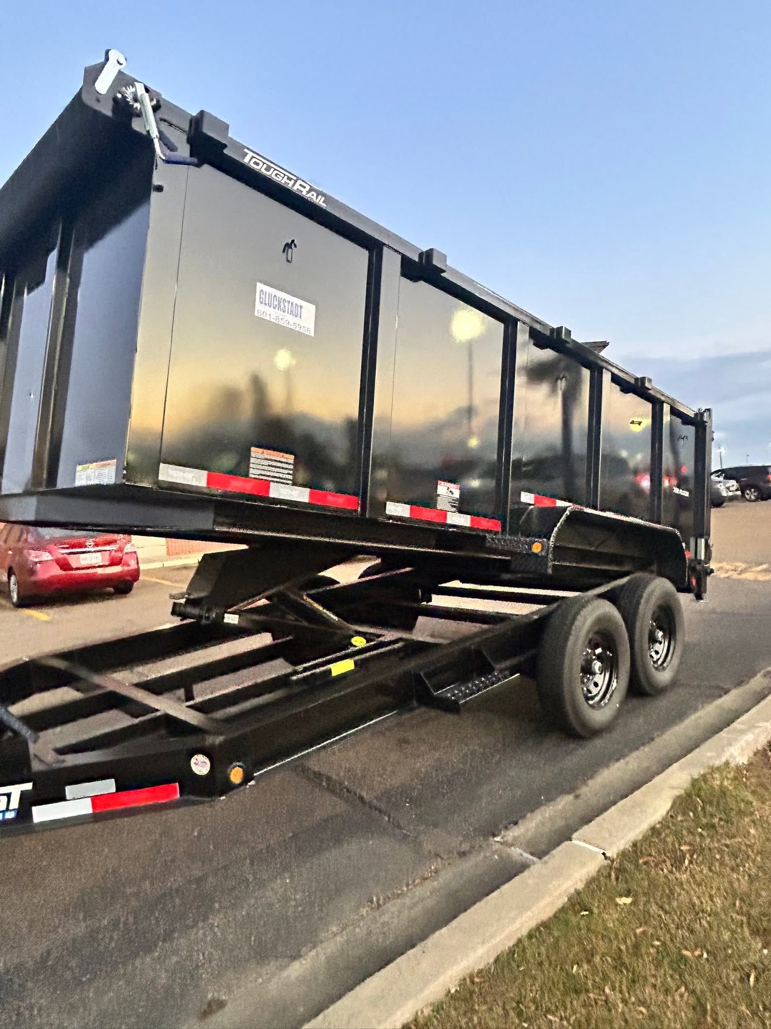 Black dump trailer on a tilted tow truck ramp beside a road under a clear sky