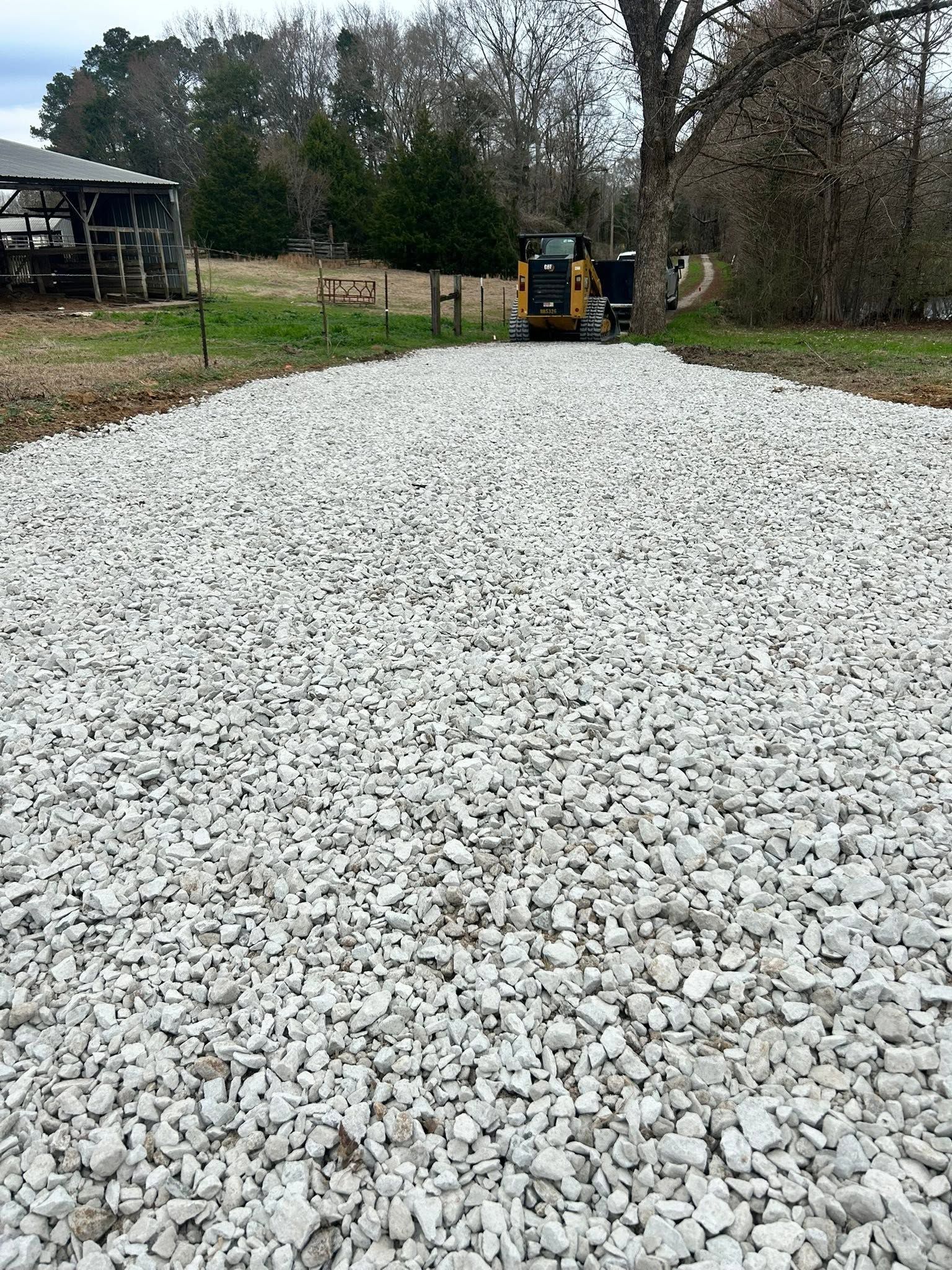 Large pile of white gravel in a yard, with a small construction vehicle in the background.