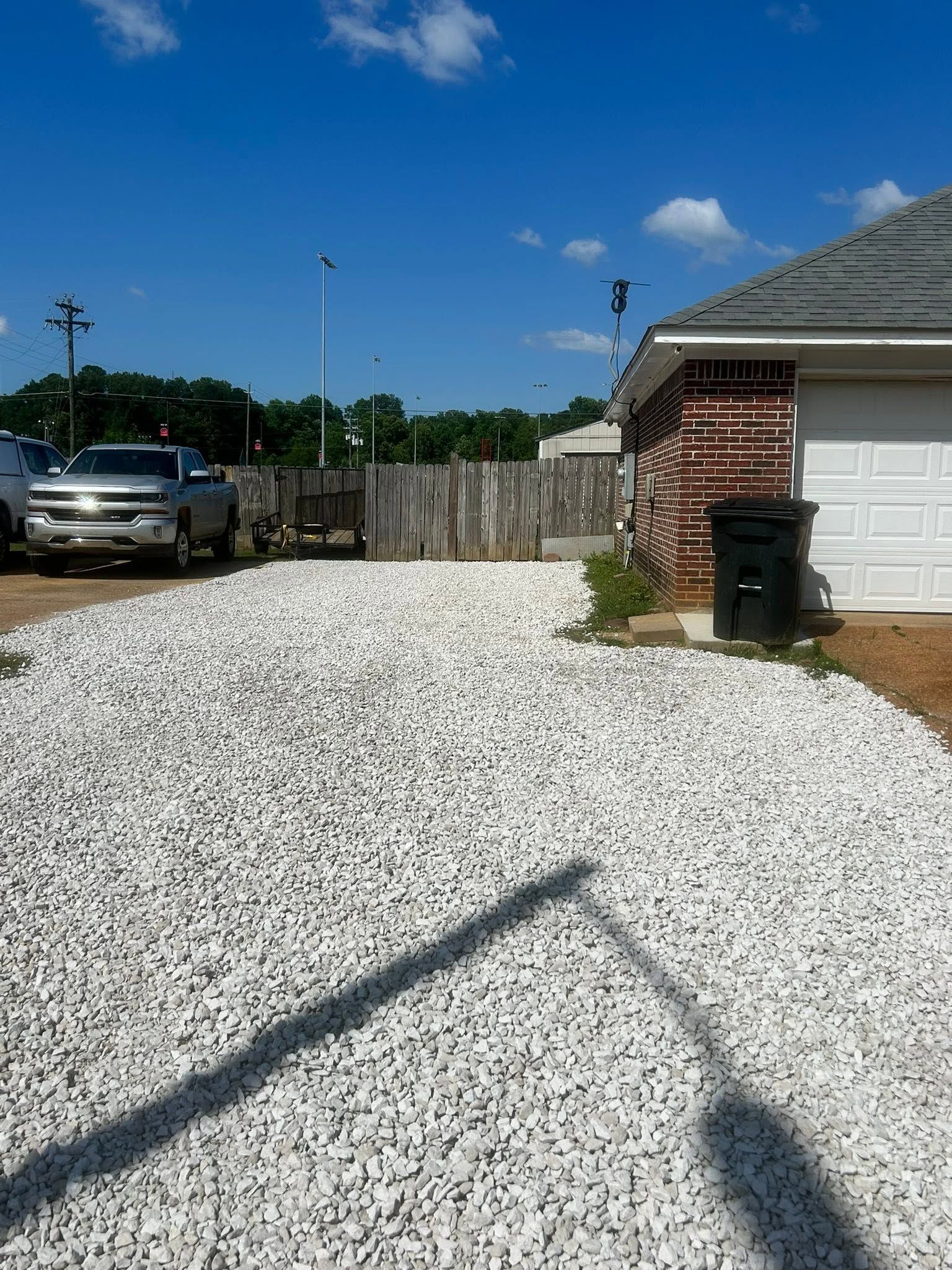 Gravel driveway beside a brick house and garage under a clear blue sky, with a parked truck and wooden fence.