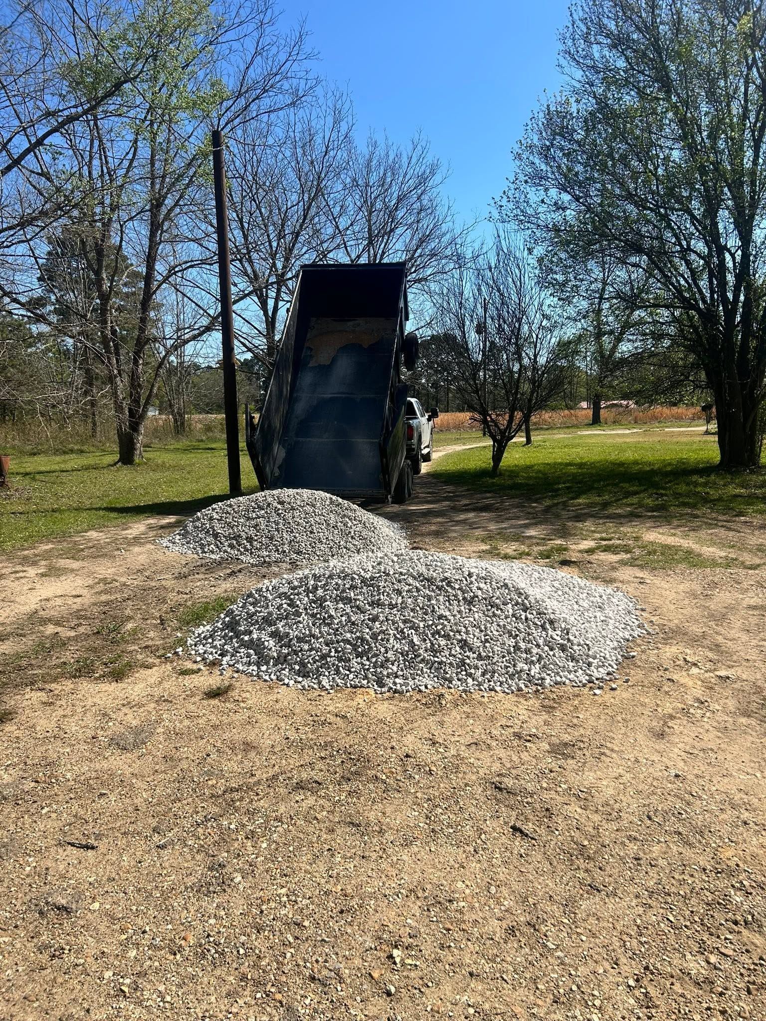 Gravel pile beneath a black dump truck at a sunny construction site with trees in the background