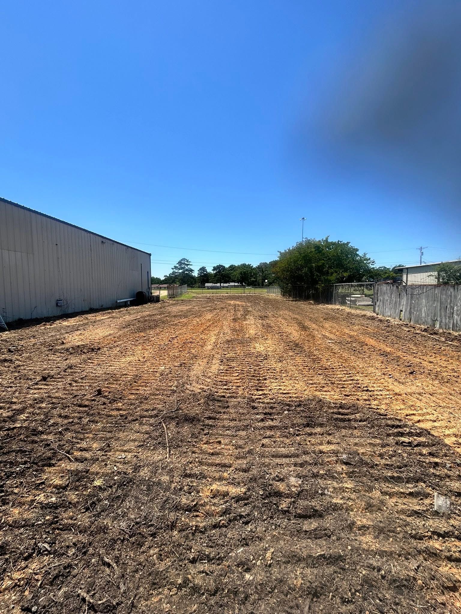 Woodchip-covered path or lot between industrial buildings under a clear blue sky.