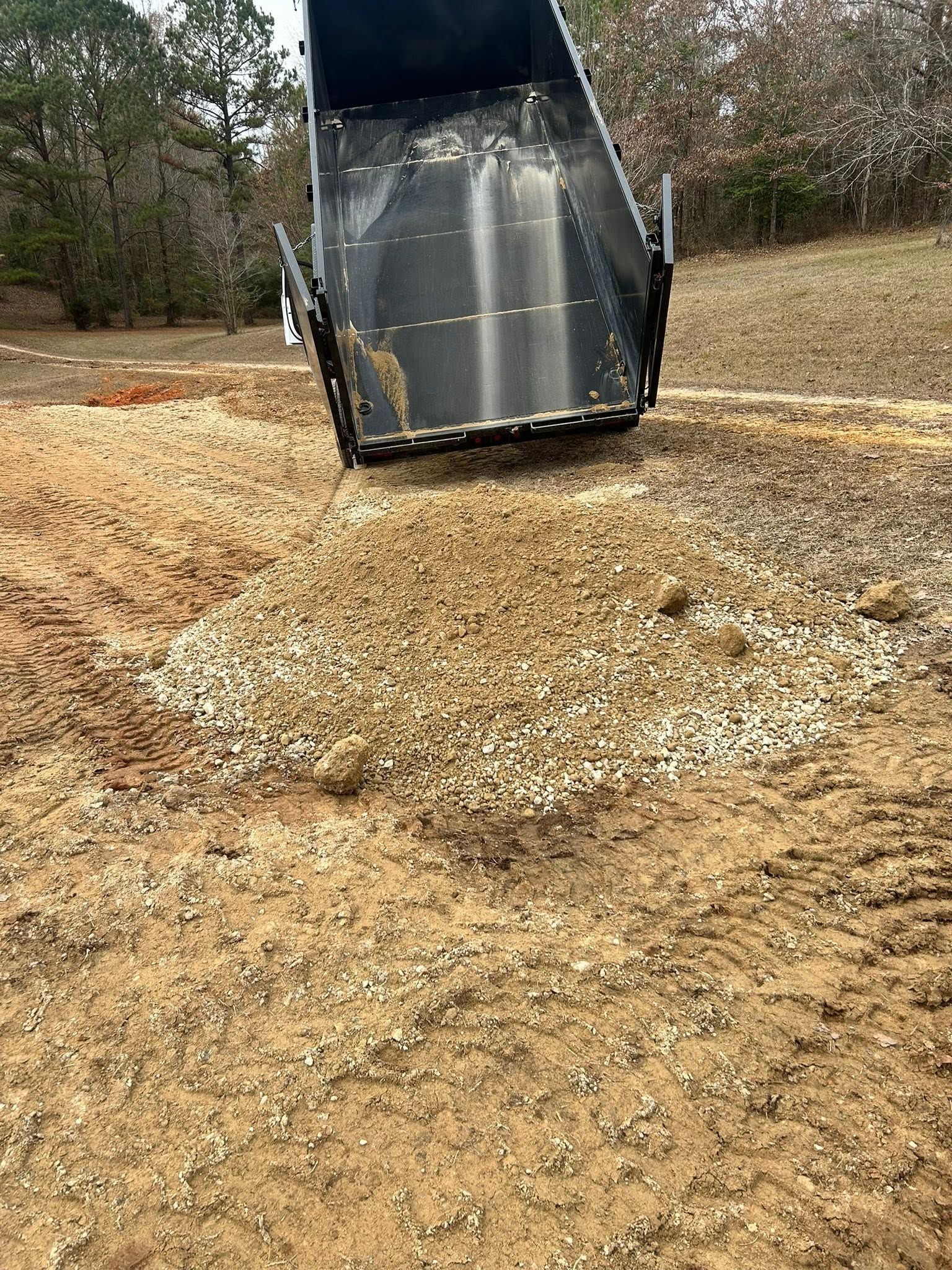 Dump truck unloading gravel onto a dirt road in a wooded area