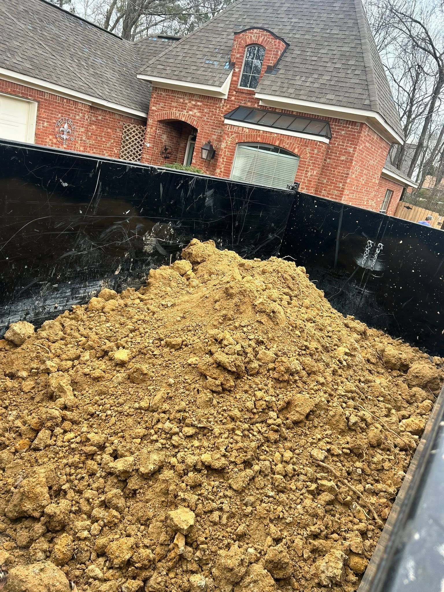 Black truck bed filled with dirt in front of a brick house under rainy sky