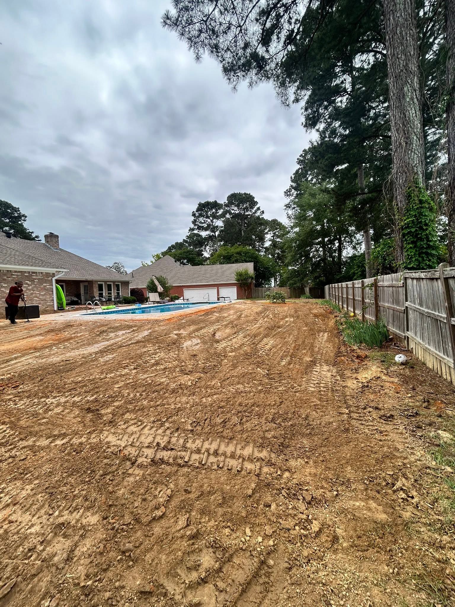 Large pile of mulch in a backyard, with houses, trees, and a cloudy sky in the background.