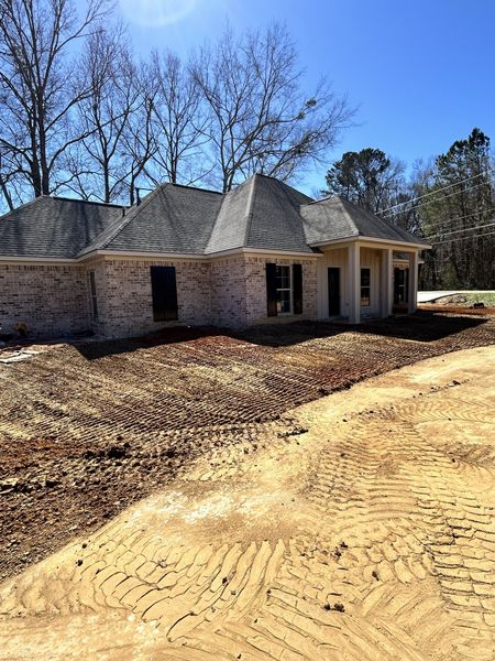 Partially built brick house with a gray shingled roof on a dirt lot under a blue sky