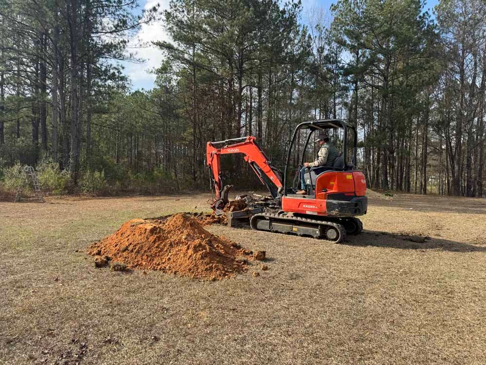 Orange excavator digging a dirt pile in a clearing with pine trees in the background