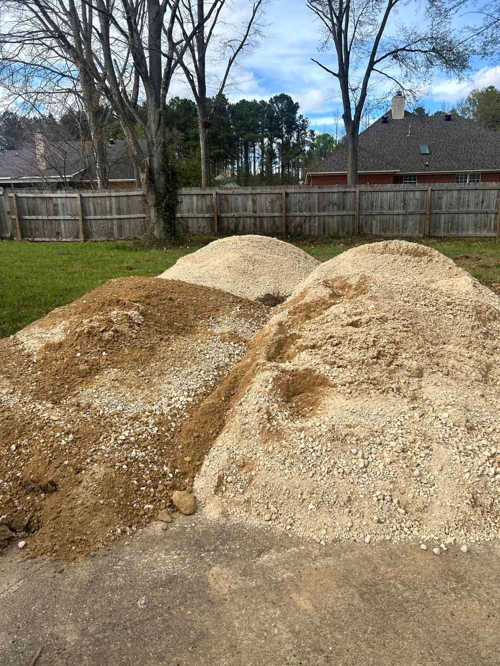 Three large piles of wood chips in a fenced backyard under a partly cloudy sky
