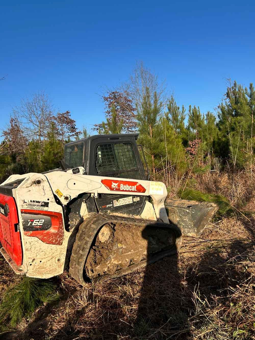 Muddy red-and-white skid steer in a field under a clear blue sky
