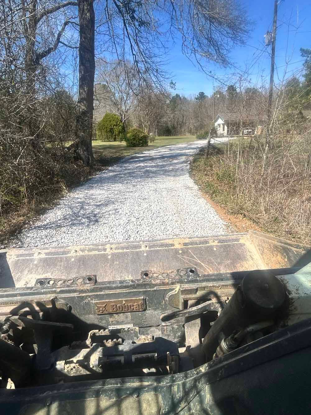 View from a vehicle on a gravel driveway curving through leafless woods on a sunny day