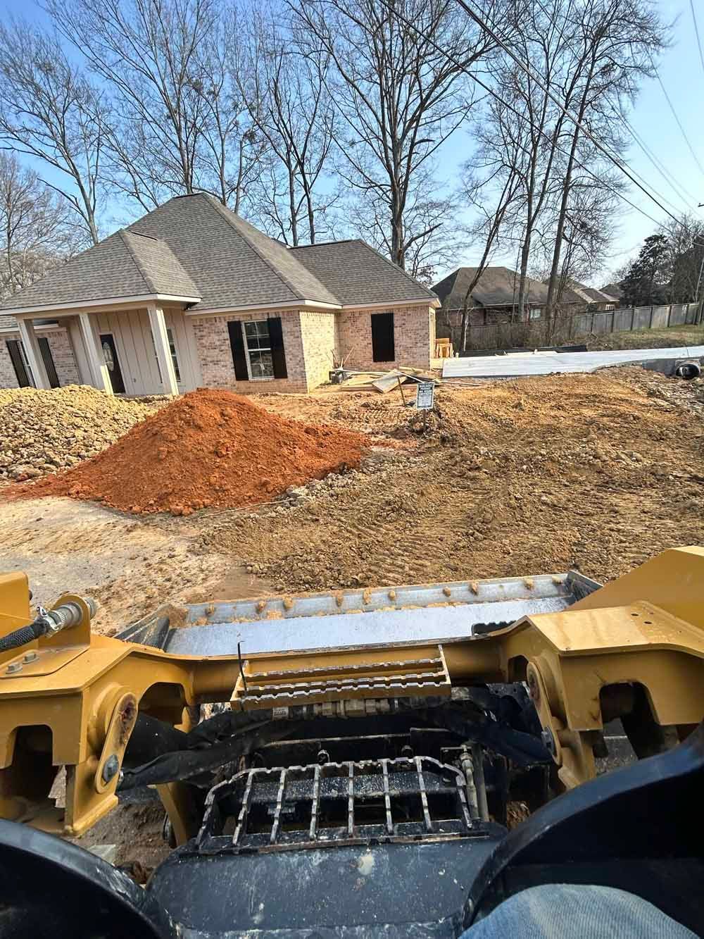 Bulldozer view of a house lot with dirt piles and a newly built home in the background
