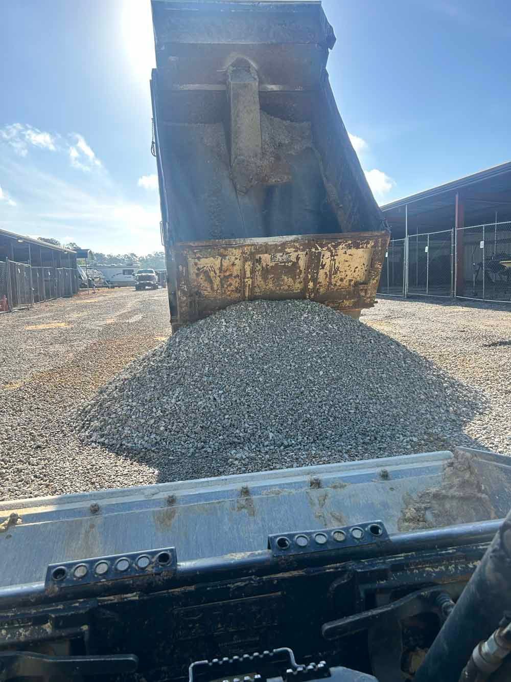 Front loader dumping a pile of gray gravel in a yard under a bright sky