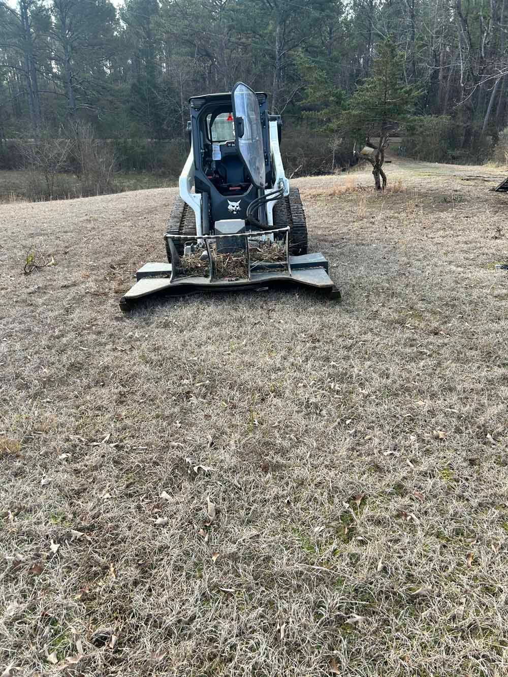 Compact tracked mower working in a grassy field with trees in the background