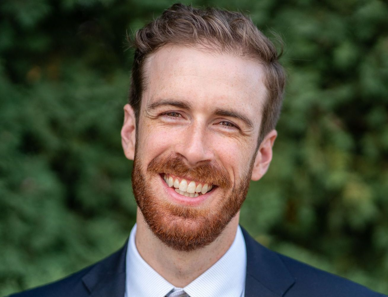 A man with a beard is wearing a blue suit and a blue shirt.