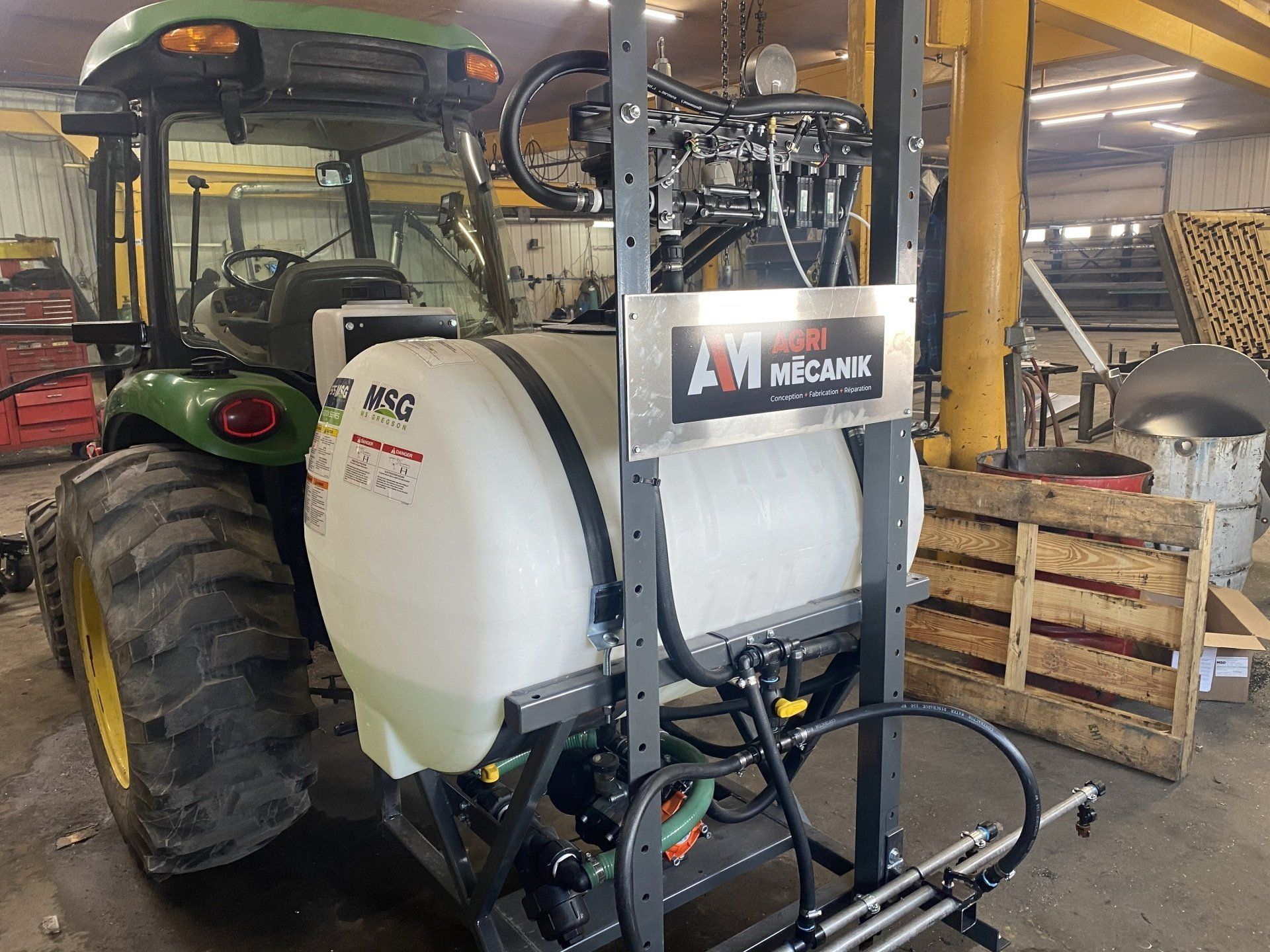Un tracteur vert est garé dans un garage avec un pulvérisateur qui y est attaché.