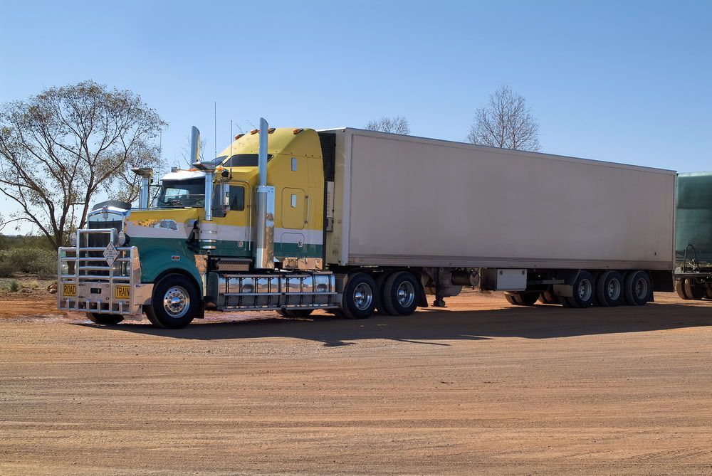 A Yellow And Green Semi Truck Is Parked On A Dirt Road — Castledine's Truck Painting & Repairs in Fountaindale, NSW