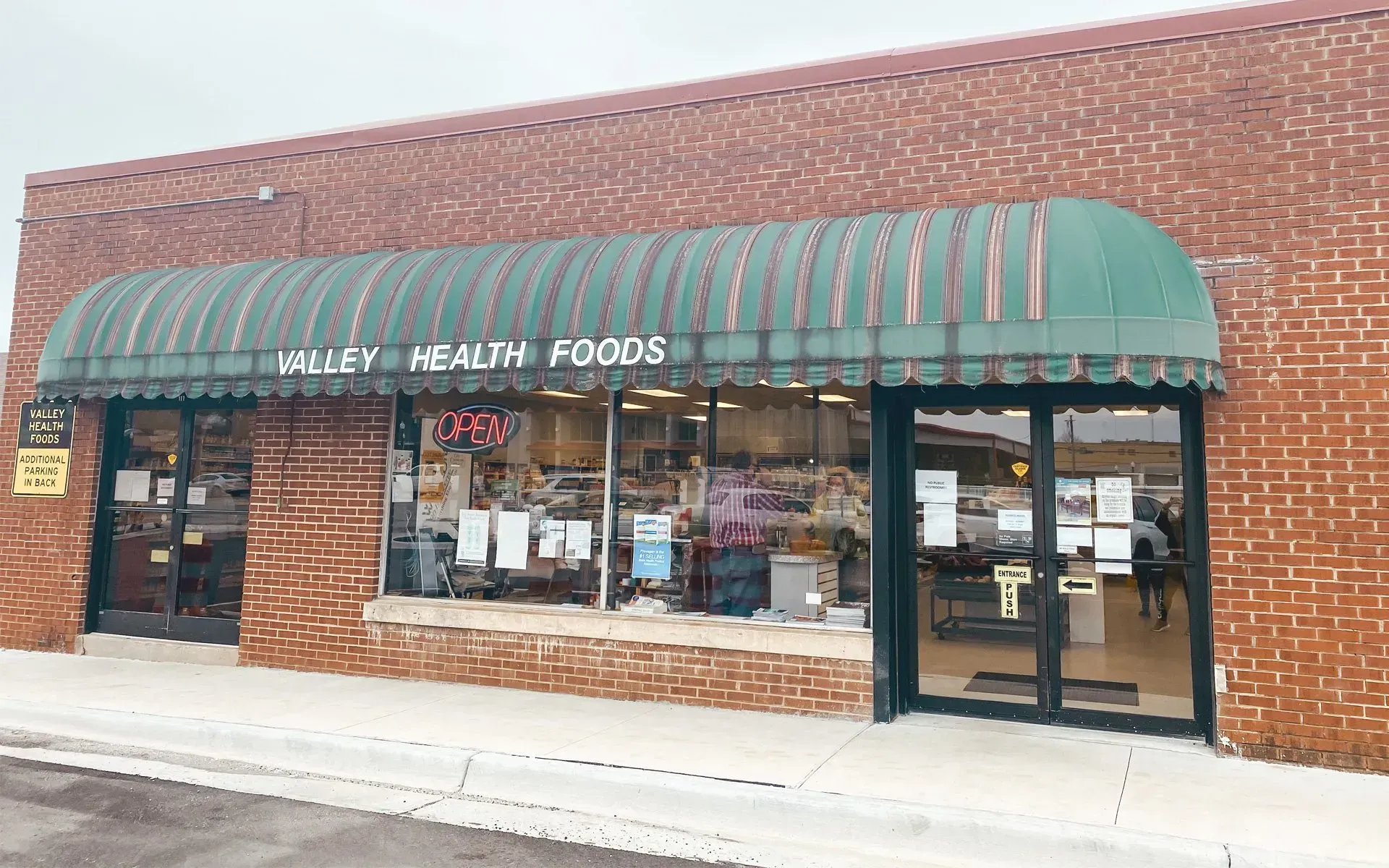 Valley Health Foods store with green awning, brick exterior, and glass windows. Valley Health Foods store with green awning, brick exterior, and glass windows.