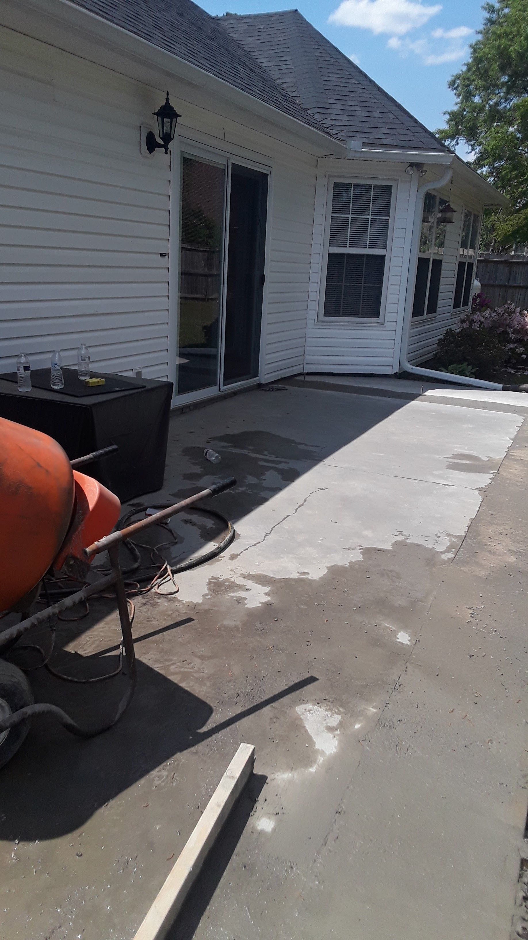 A white-sided house with a concrete patio under construction, featuring a cement mixer in the foreground.