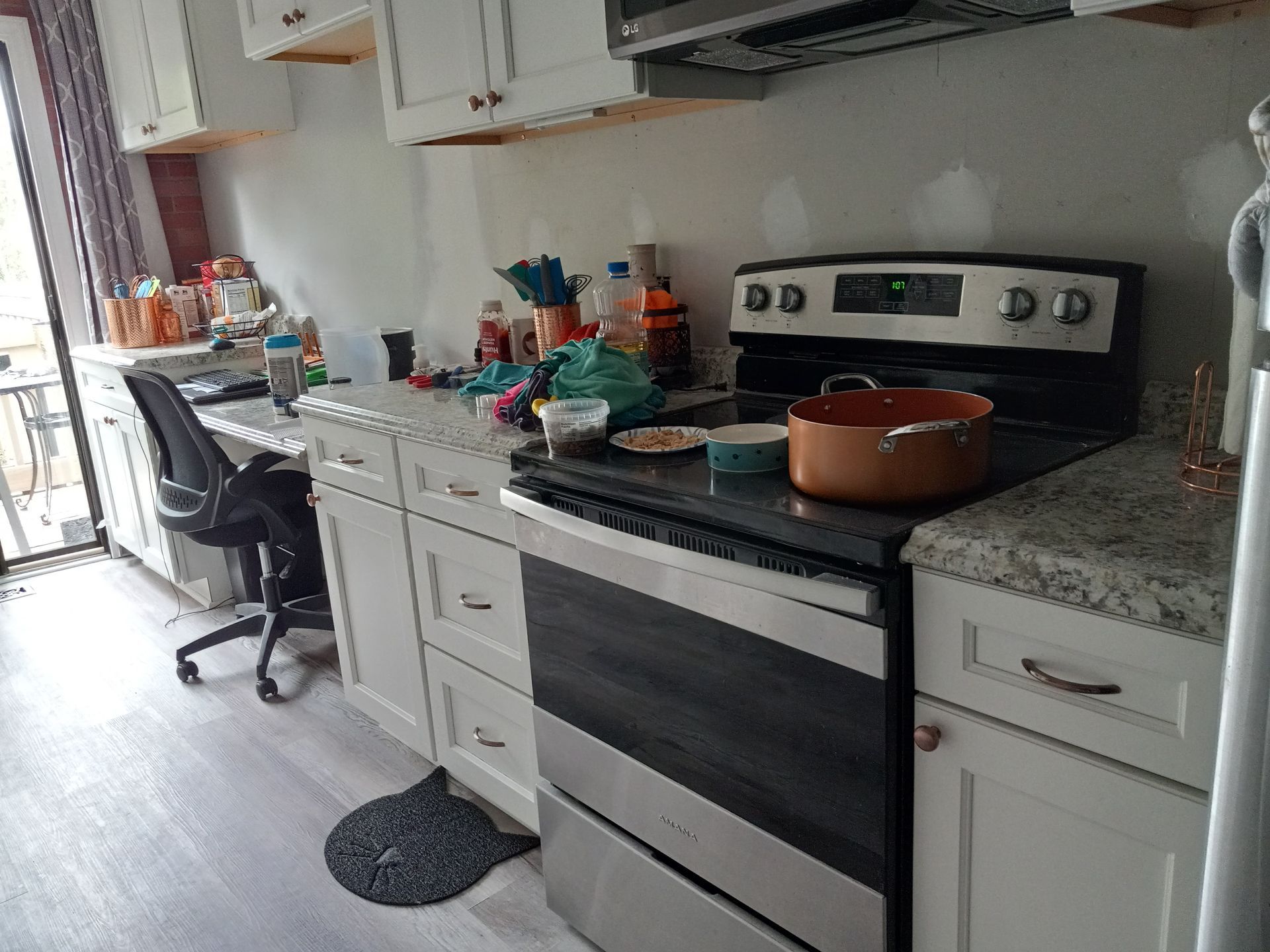 A kitchen with white cabinets, light countertops, a stainless steel stove with a pot, and a black office chair.