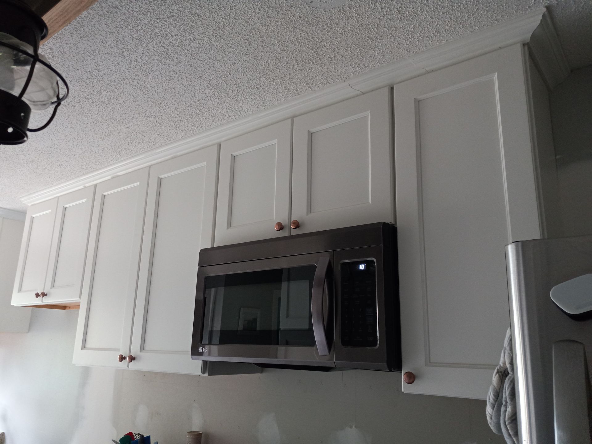 White kitchen cabinets with a dark microwave mounted underneath, set against a textured ceiling.
