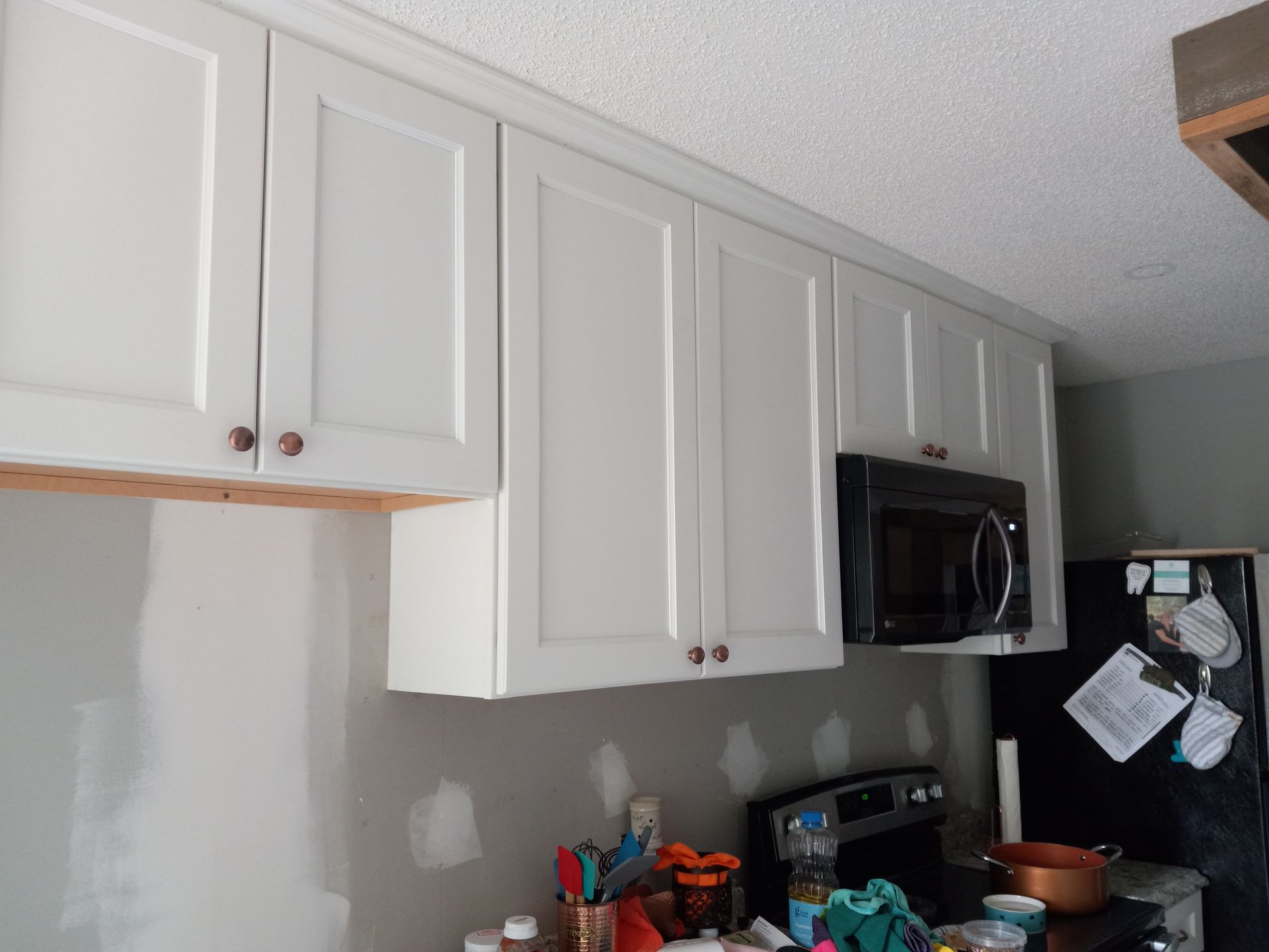 White kitchen cabinets installed above a countertop with a microwave and a partially finished wall.