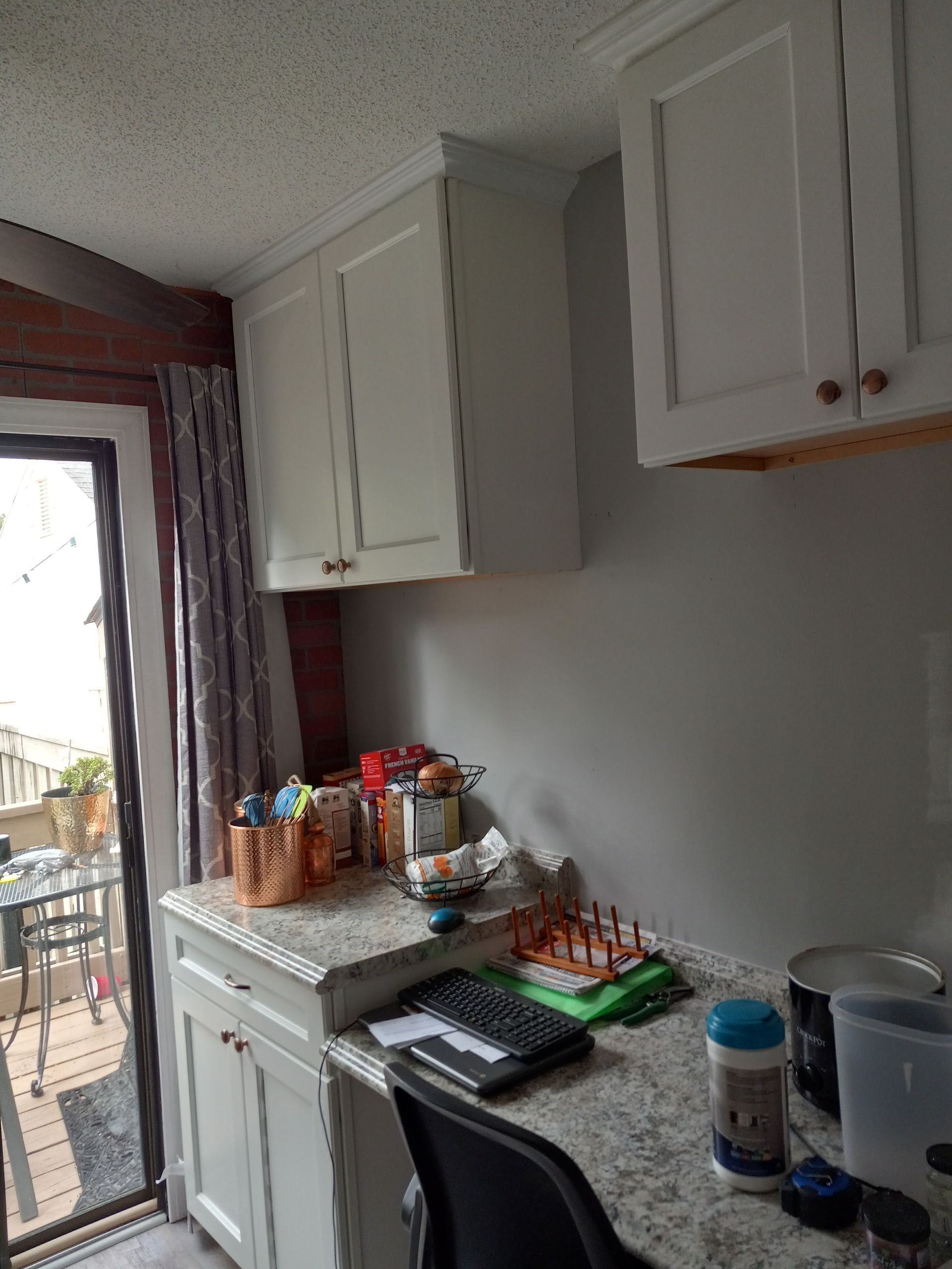 A kitchen corner with white cabinets, a speckled countertop, a clutter of items, and a glass door leading to a patio.