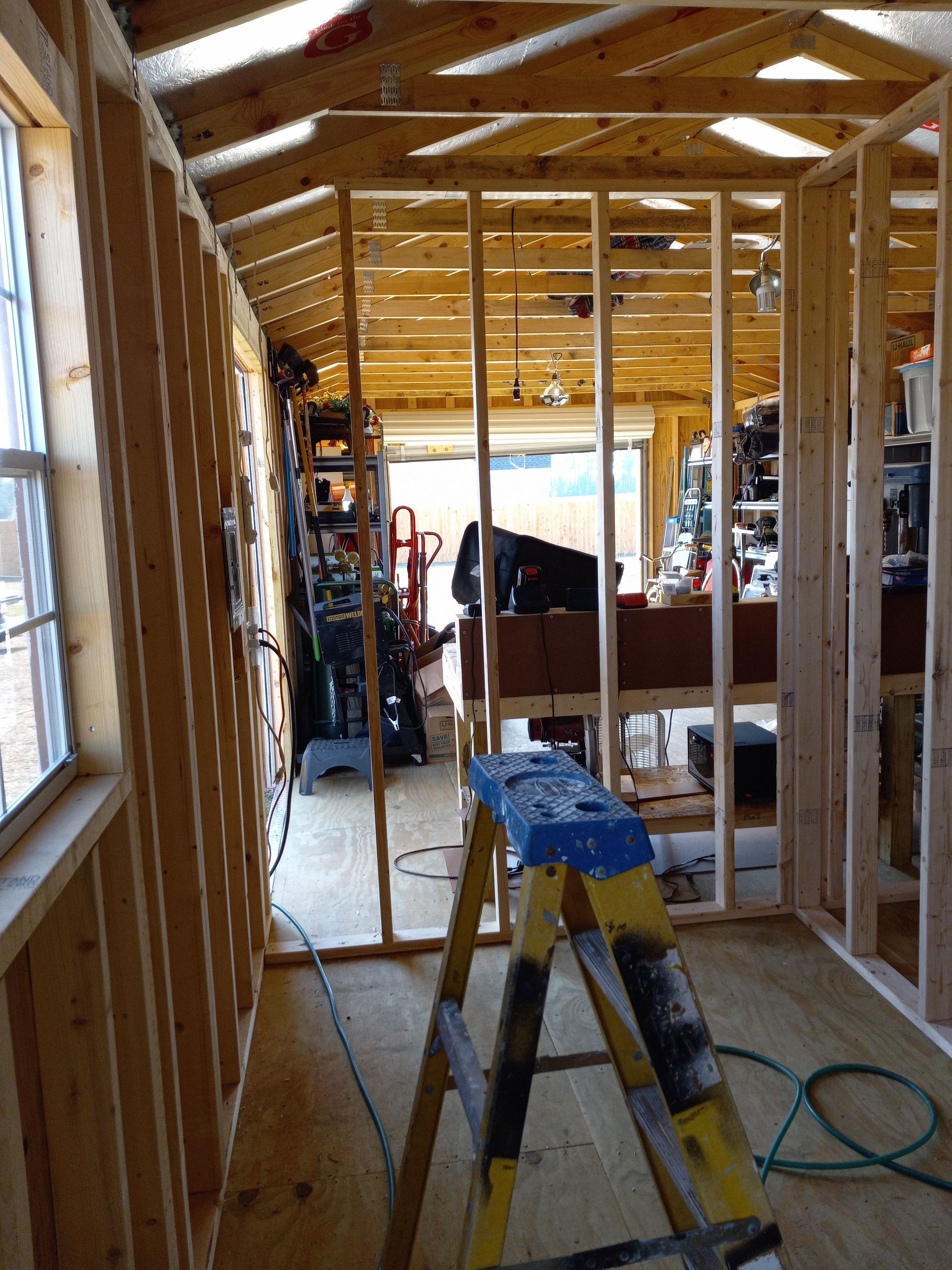 The interior of an unfinished wood-framed building under construction, with a yellow stepladder in the foreground.