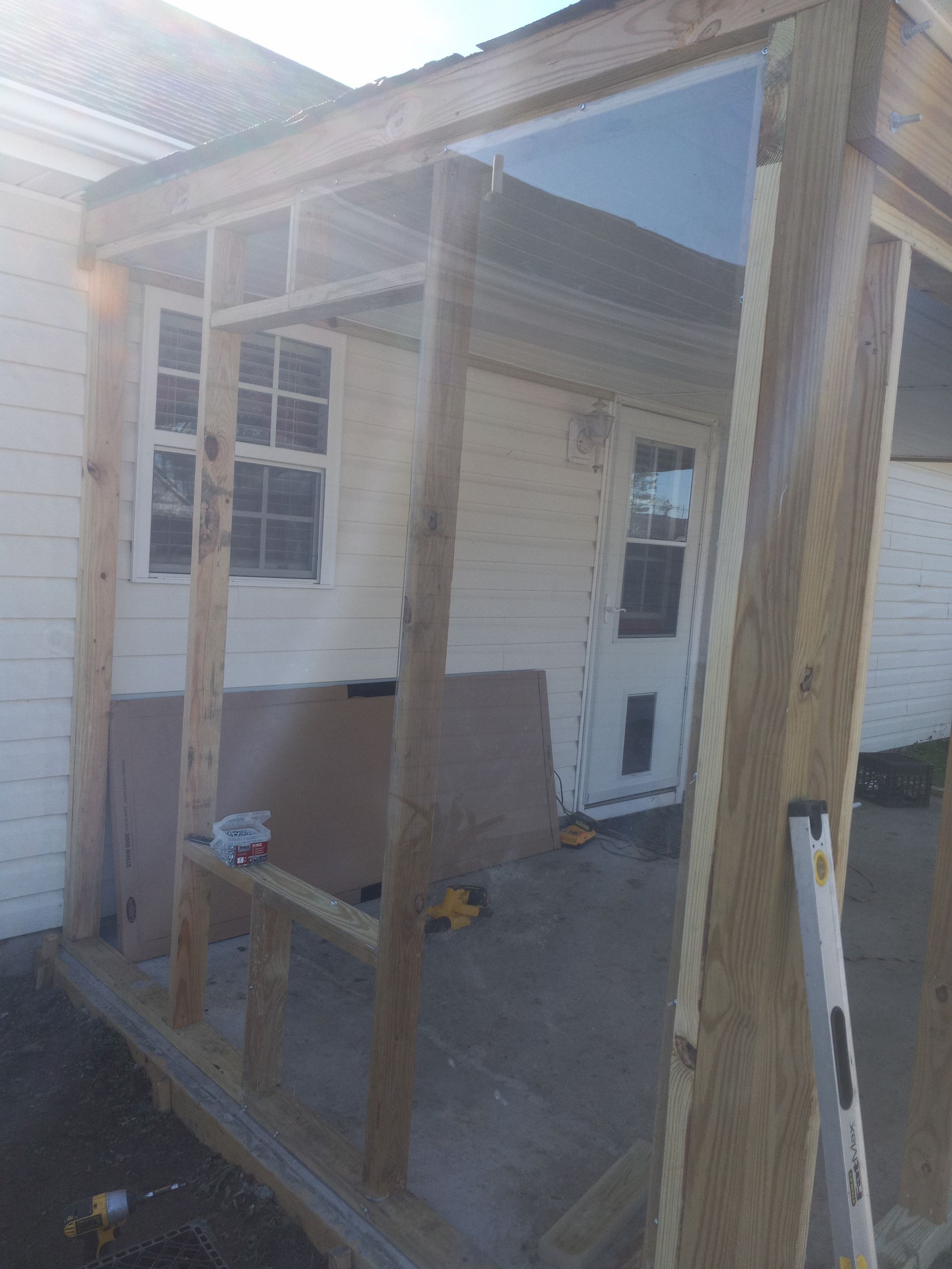 A wooden porch frame under construction, attached to the white siding of a house with visible windows and a door.