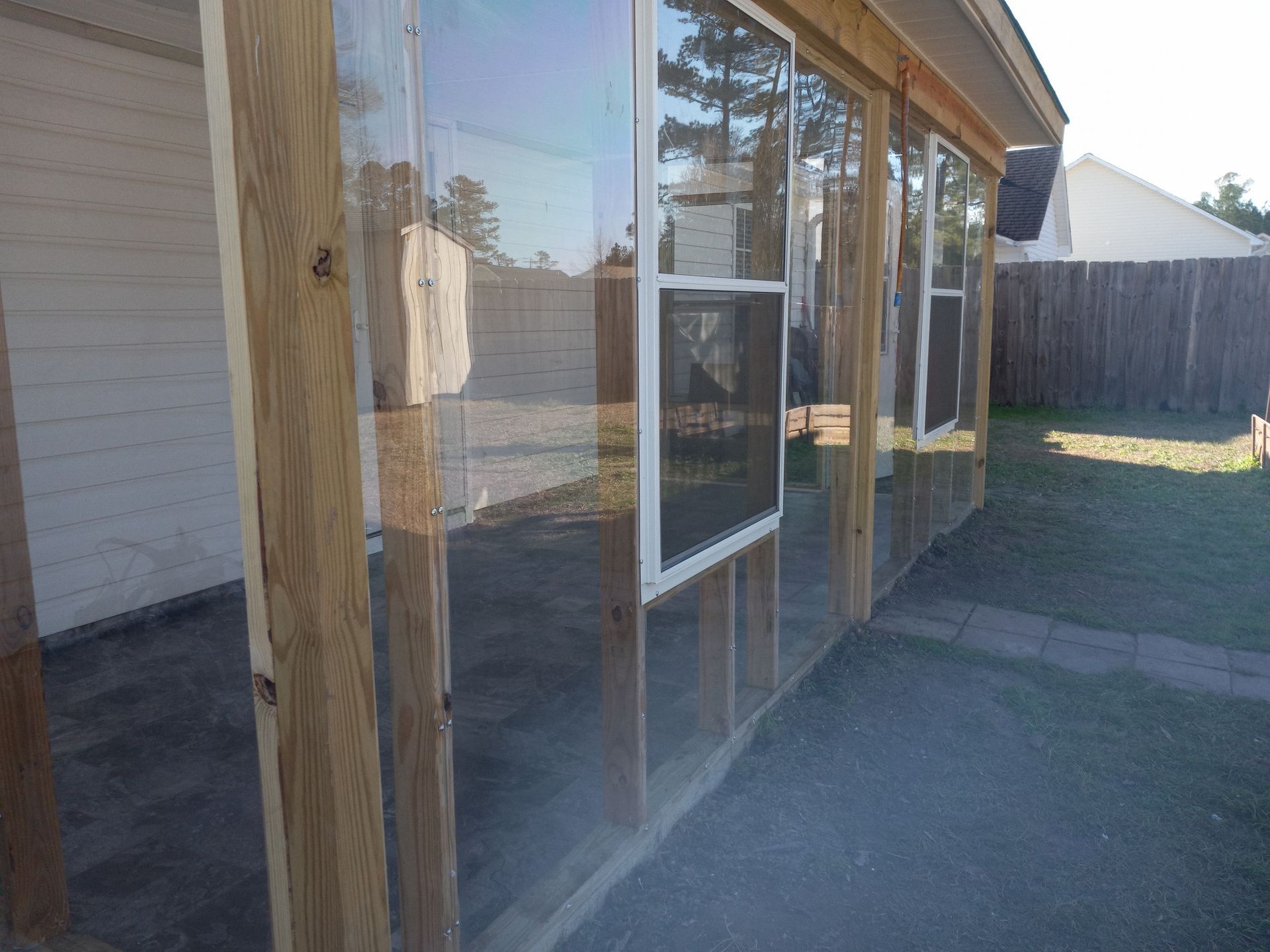 A side view of a porch enclosure featuring wooden posts, clear vinyl panels, and installed window units.