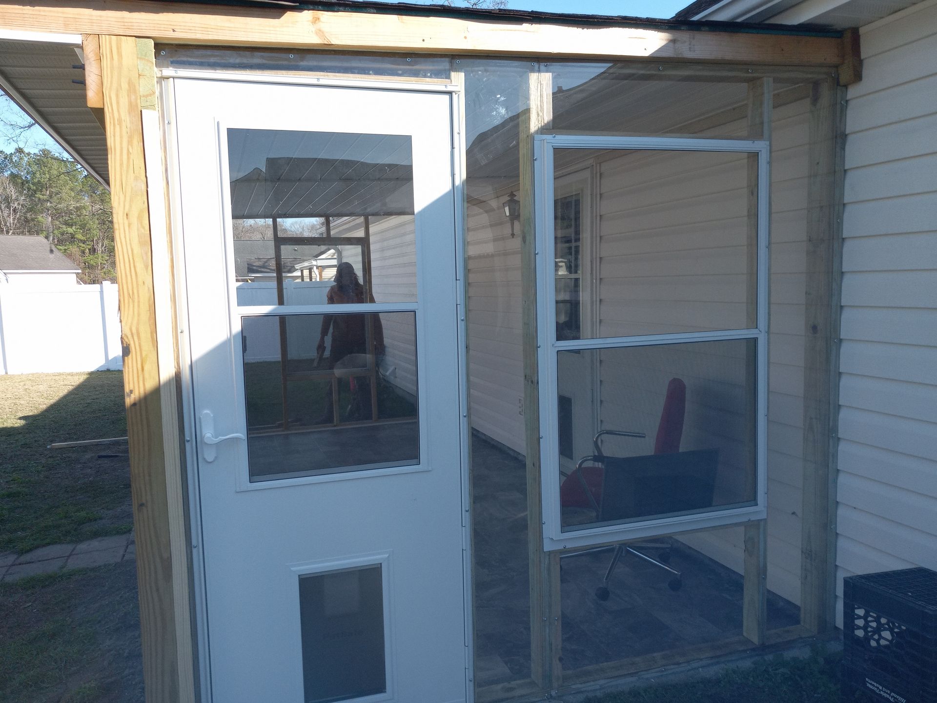 A white door with a pet flap and a single-hung window installed in a partially finished wooden porch frame.
