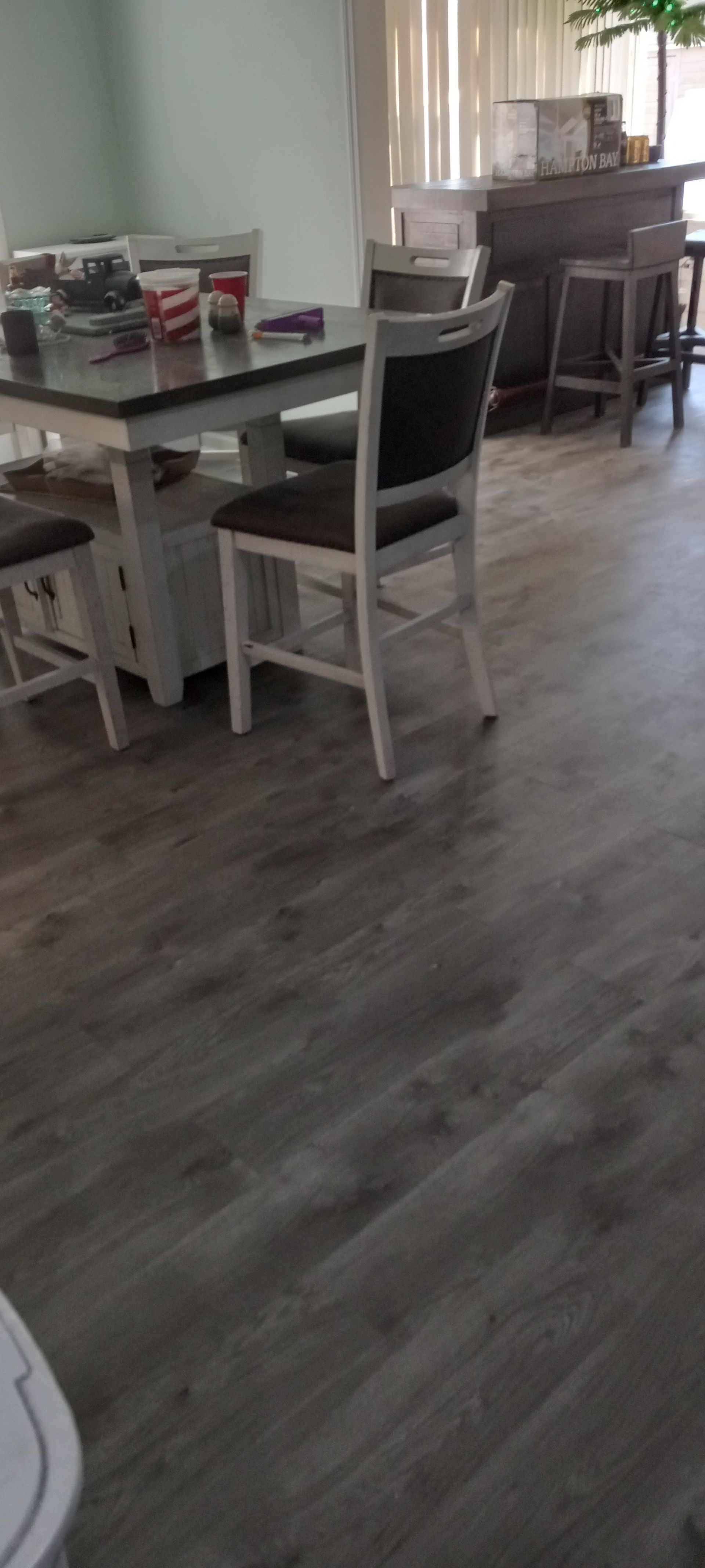A dining area with a white wooden table and chairs on grey wood-plank flooring, with a kitchen counter visible behind.