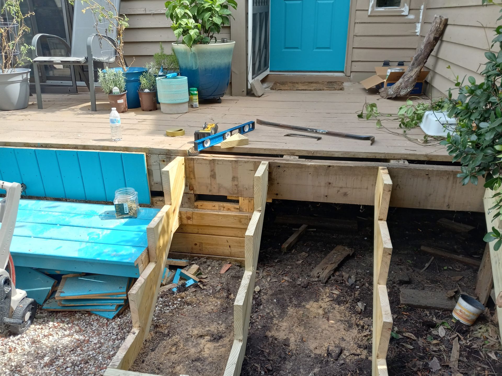 Exterior view of a home entrance with an unfinished wooden staircase under construction and a vibrant blue door.