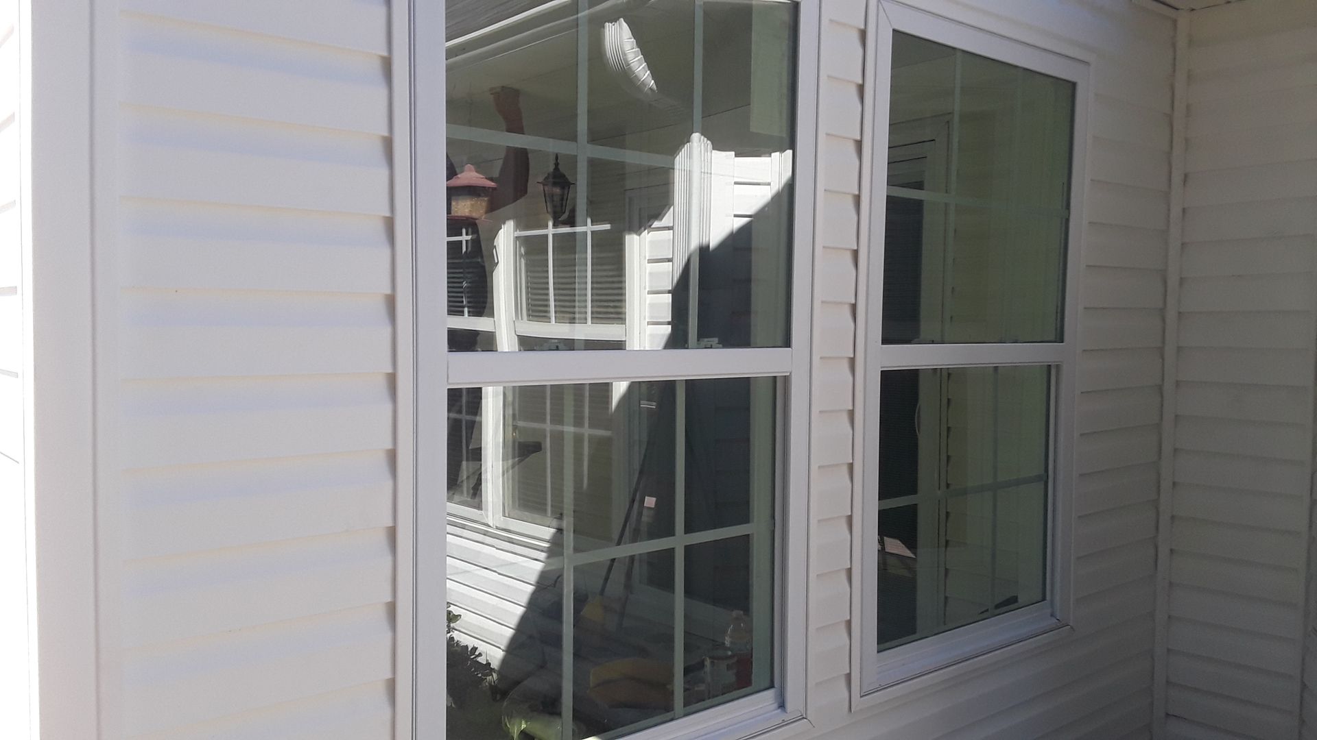 A white-framed window on a building with white horizontal siding, featuring a grid pattern on the left pane.
