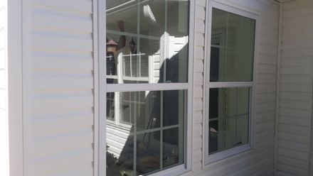 A white-framed window on a building with white horizontal siding, featuring a grid pattern on the left pane.