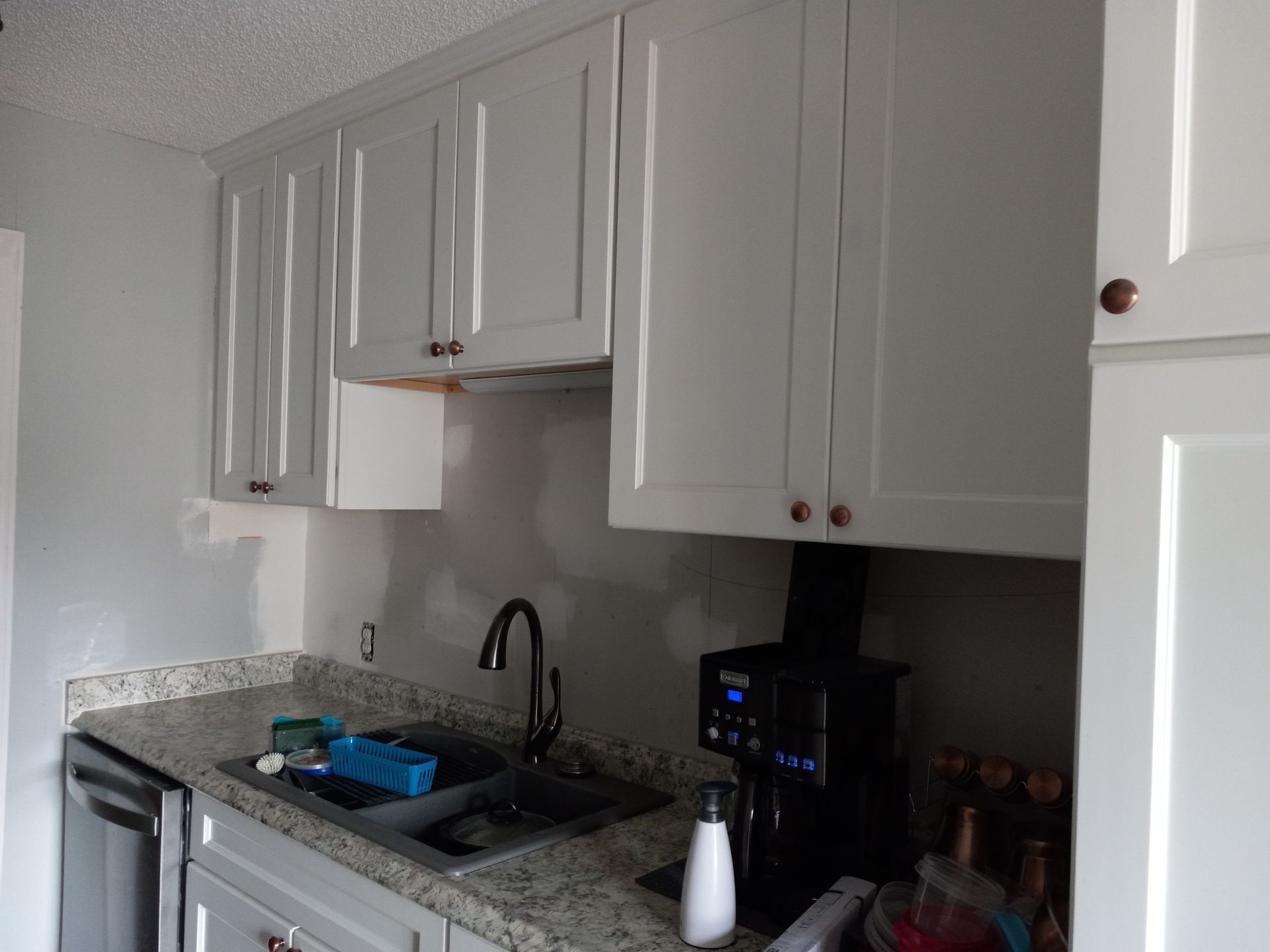 A kitchen counter with grey cabinets, a sink, a coffee maker, and stone-patterned countertops.