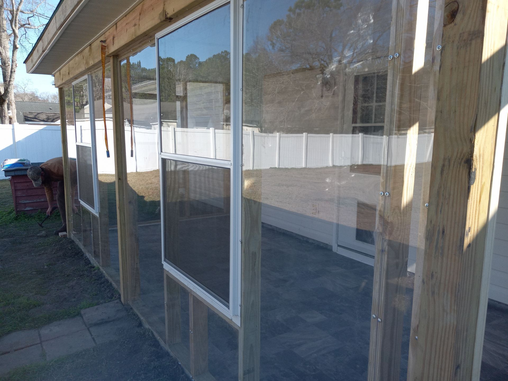 A partially enclosed patio featuring wooden framing and clear vinyl weather curtains with mounted windows.