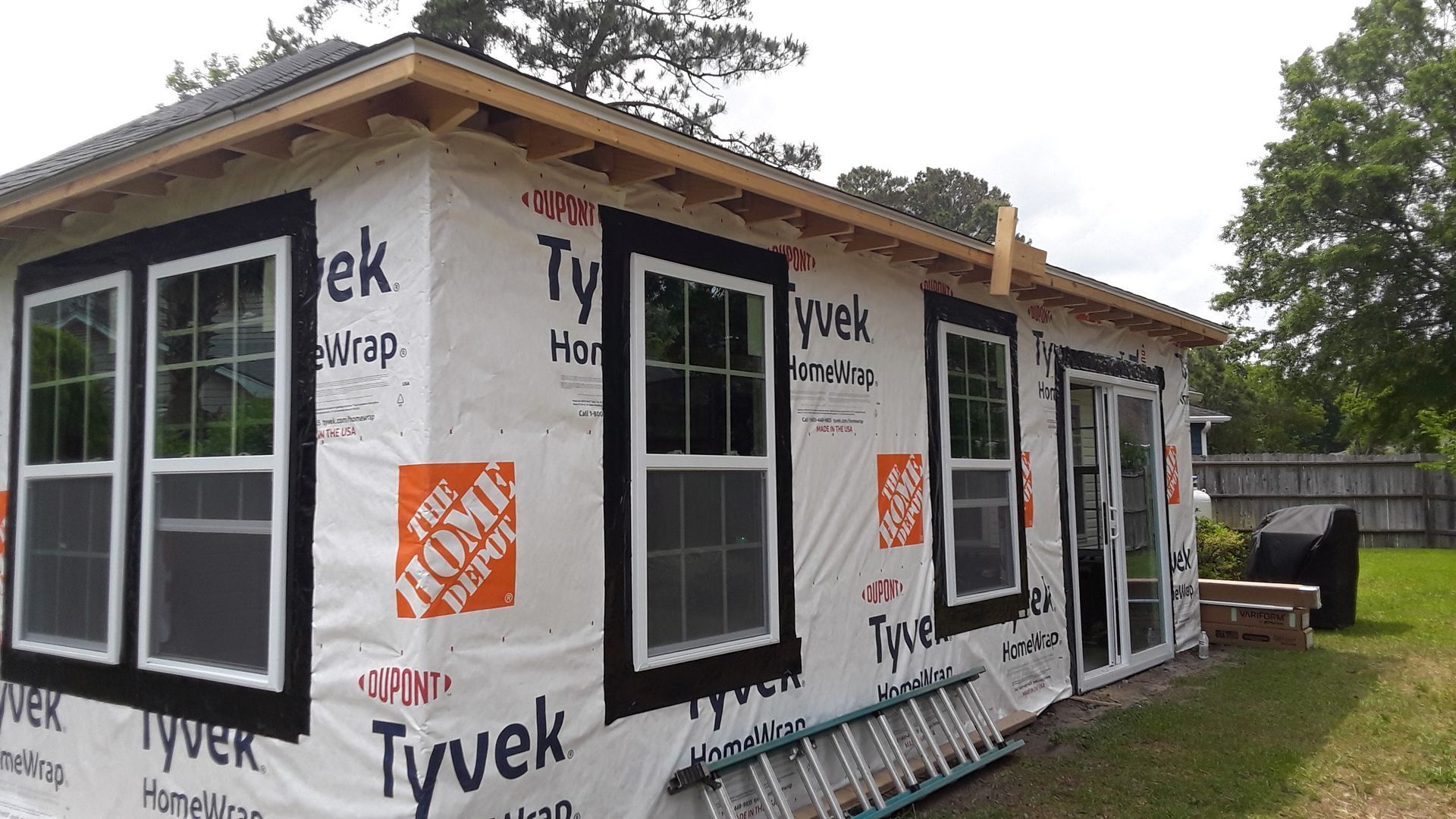 A structure under construction with black-trimmed windows and doors, wrapped in white Tyvek house wrap.