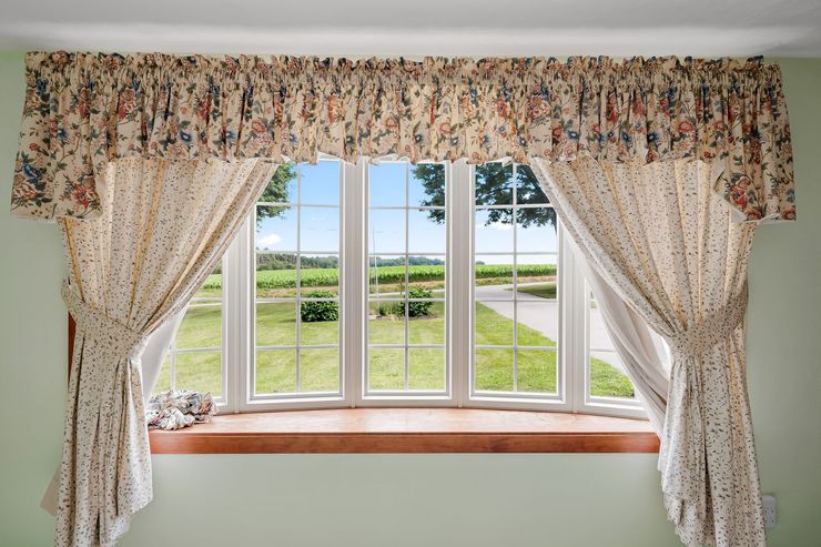 2014 Peterman Rd Property - floral curtains framing a bay window with a view of green fields and a driveway outside