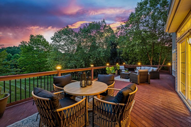 803 Zenith Dr Property - deck with wicker patio furniture overlooking trees at sunset, with a colorful sky and warm lights