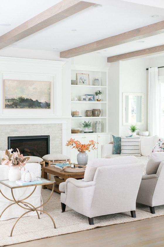 Bright living room with white furniture, a fireplace, built-in shelves, and exposed ceiling beams