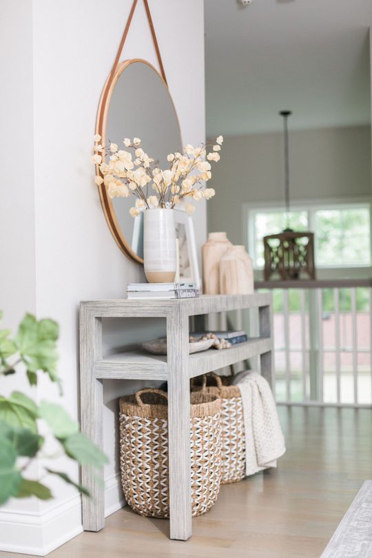 Stylish hallway console with oval mirror, white vases, wicker basket, and greenery in a bright home interior