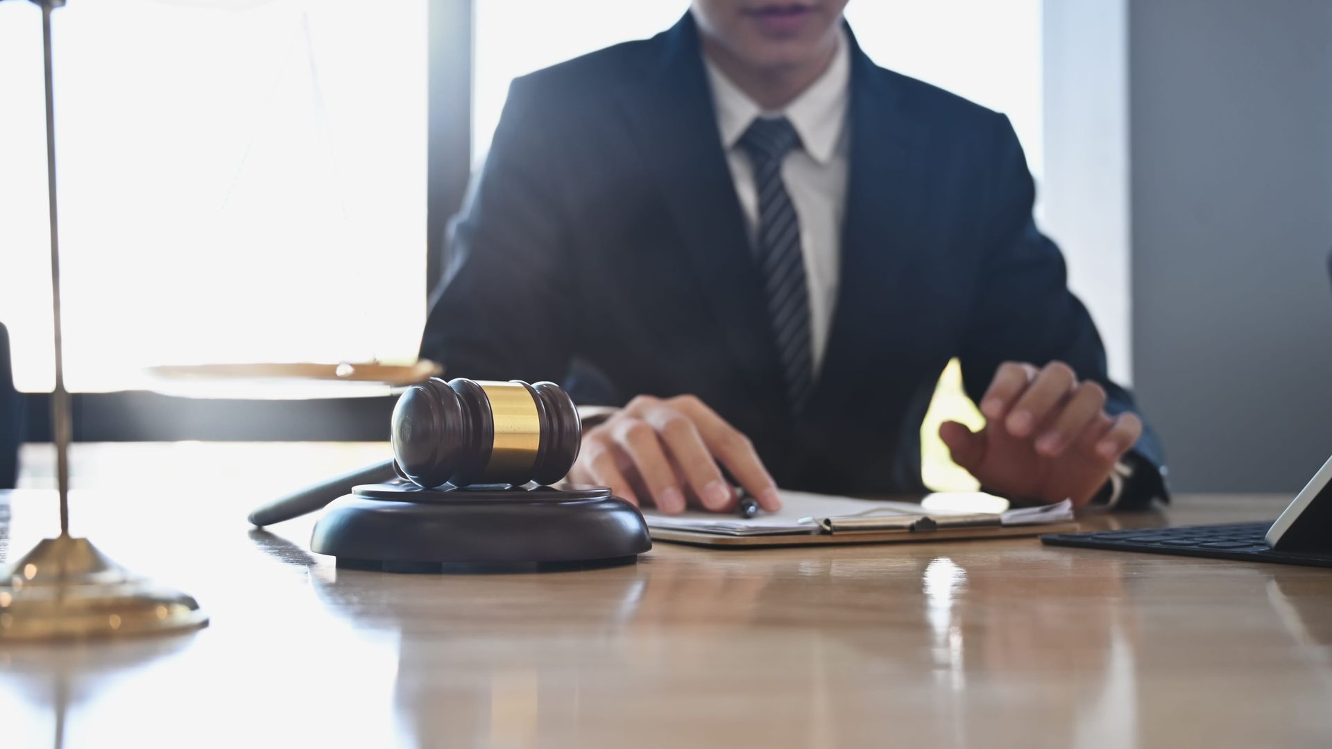 Business person at desk with gavel and laptop, signing documents in a bright office