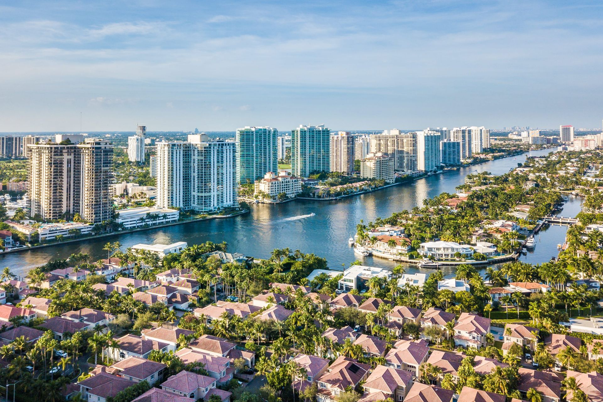Aerial view of a waterfront city with high-rise buildings, canals, and palm-lined neighborhoods under a clear blue sky