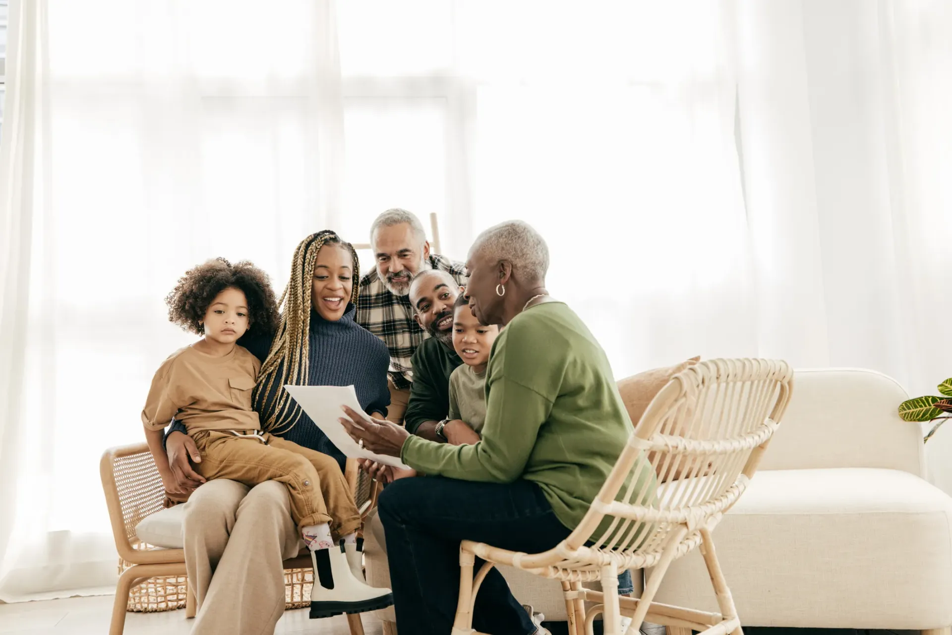 Family gathered indoors, looking at document; smiling.