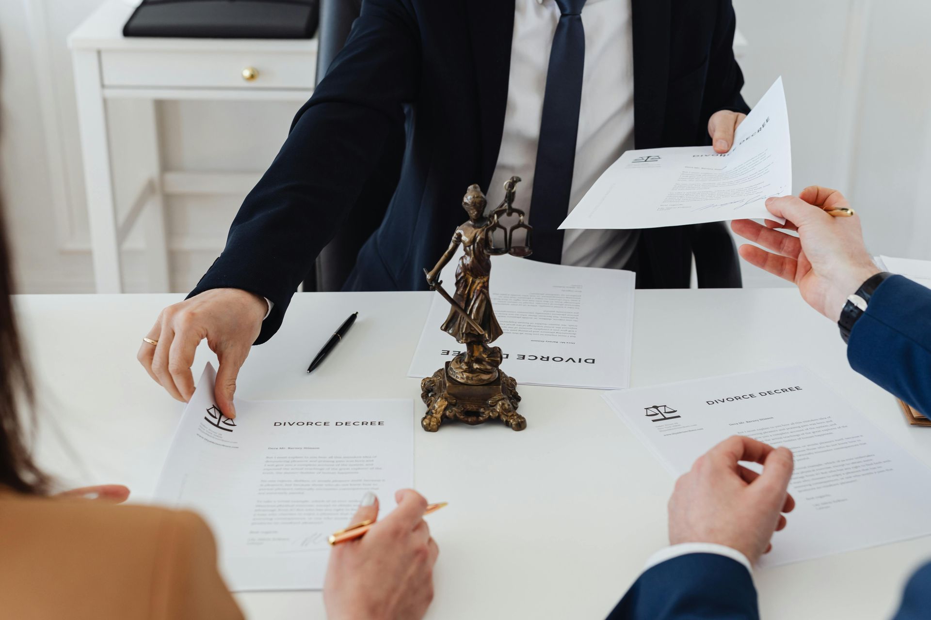 Lawyer handing documents to a couple at a desk with a Lady Justice statue.