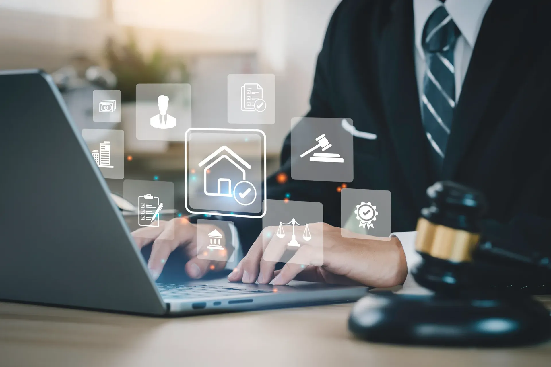 A person in a suit types on a laptop, with digital icons overlaid, including a house icon. A gavel rests on the desk.