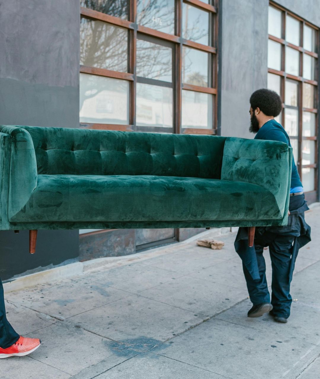 A man is carrying a green couch down a sidewalk