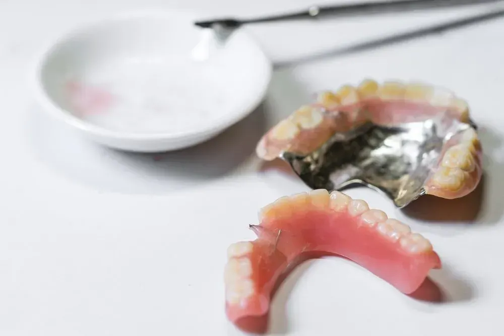 A Denture is Sitting on a Table Next to a Bowl and a Pair of Tweezers — Twin Towns Denture Clinic In Forster, NSW